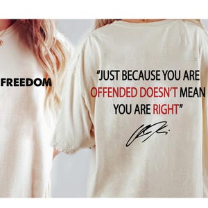 May include: Two cream-colored t-shirts. One shirt has the word "FREEDOM" printed in black. The other shirt has the quote "JUST BECAUSE YOU ARE OFFENDED DOESN'T MEAN YOU ARE RIGHT" printed in black and red, with a signature.