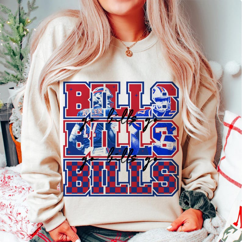 May include: A beige sweatshirt with a graphic design featuring the word "BILLS" in red and blue, with images of football players. The design includes the text "Bills go Bills" in a script font.