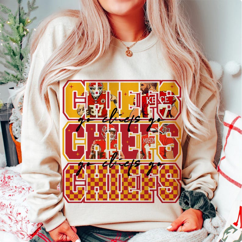 Peut inclure: Un sweat-shirt cr&egrave;me avec un motif graphique rouge et or. Le motif pr&eacute;sente le mot "CHIEFS" et la phrase "go chiefs go", ainsi que des images de joueurs de football.
