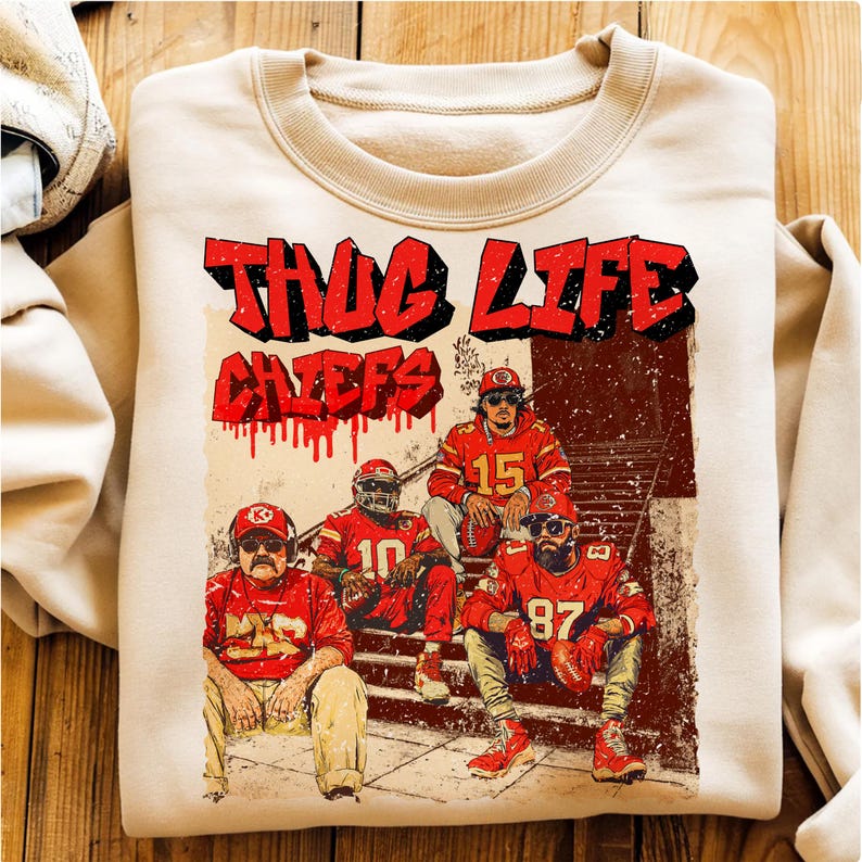 May include: Cream-colored sweatshirt featuring a graphic of four football players in red uniforms, with the text "THUG LIFE CHIEFS" in red and black. The design has a distressed, vintage look, with a grunge aesthetic.