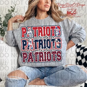 May include: A grey sweatshirt featuring the word "PATRIOTS" in red, white, and blue block letters. The design includes the phrase "go patriots go" and images of football players. The sweatshirt is a casual style.