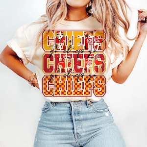 Peut inclure: T-shirt cr&egrave;me avec un motif graphique rouge et or. Le motif pr&eacute;sente le mot "CHIEFS", des images de joueurs et l'expression "go chiefs go". Le motif est r&eacute;p&eacute;t&eacute; trois fois sur le devant du t-shirt.