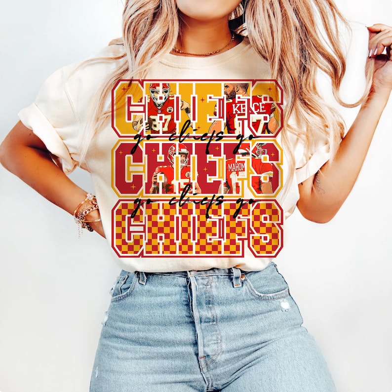 Peut inclure: T-shirt cr&egrave;me avec un motif graphique rouge et or. Le motif pr&eacute;sente le mot "CHIEFS", des images de joueurs et l'expression "go chiefs go". Le motif est r&eacute;p&eacute;t&eacute; trois fois sur le devant du t-shirt.
