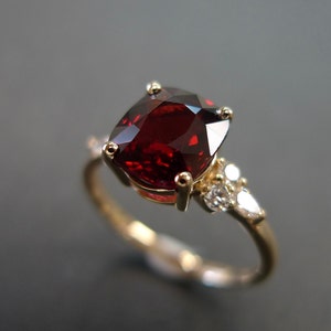 May include: A gold ring with a large, red gemstone and smaller, white gemstones on the band.