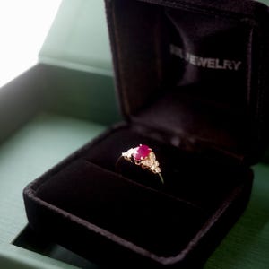 this unique natural oval ruby and marquise diamond ring is sit on a black ring box, ready for gifting.