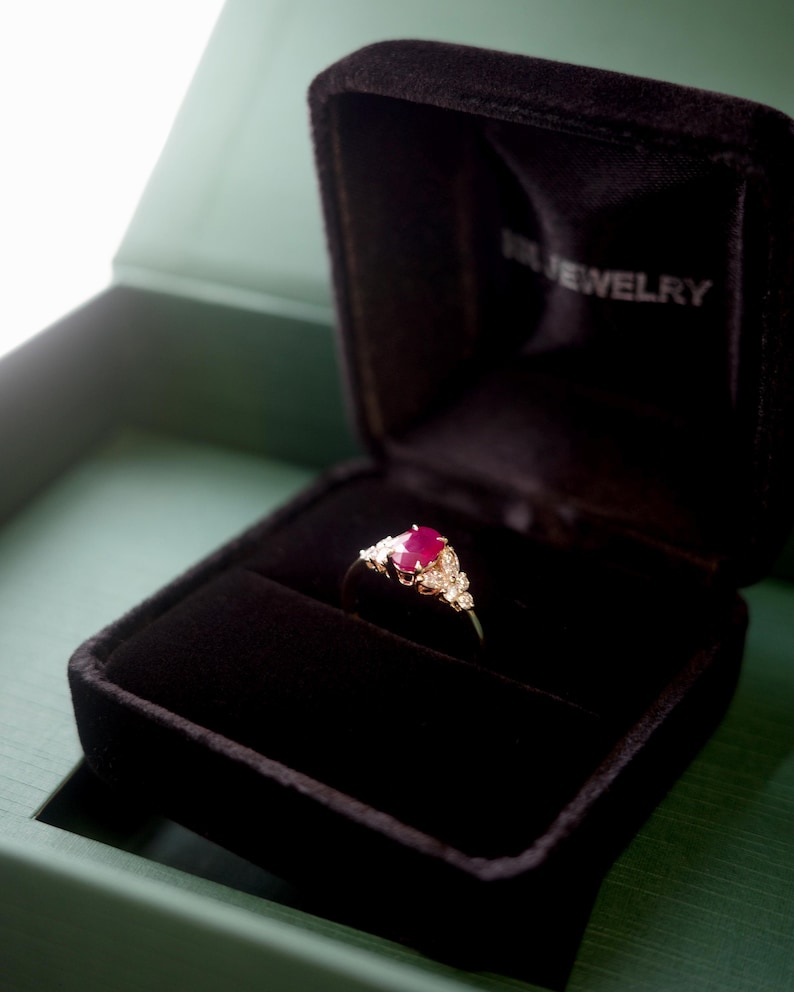 this unique natural oval ruby and marquise diamond ring is sit on a black ring box, ready for gifting.
