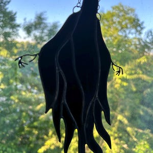 Pu&ograve; includere: Suncatcher a forma di fantasma in vetro colorato nero appeso a una catena. Il fantasma ha una veste fluente e braccia tese con dettagli delicati saldati a mano. Progettato per essere appeso a una finestra.