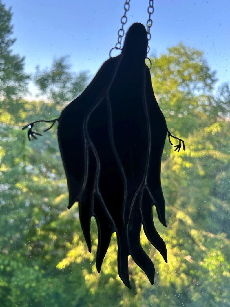 Pu&ograve; includere: Suncatcher a forma di fantasma in vetro colorato nero appeso a una catena. Il fantasma ha una veste fluente e braccia tese con dettagli delicati saldati a mano. Progettato per essere appeso a una finestra.