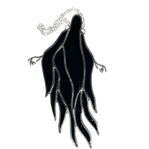 Pu&ograve; includere: Una figura di fantasma in vetro colorato nero con le braccia tese e una catena d'argento per appenderla. Il fantasma ha un design stilizzato e fluido con un bordo argentato. Progettato come un acchiappasole o una decorazione per finestre.