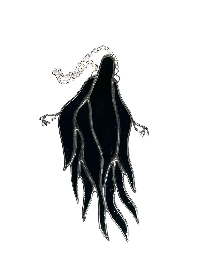 Pu&ograve; includere: Una figura di fantasma in vetro colorato nero con le braccia tese e una catena d'argento per appenderla. Il fantasma ha un design stilizzato e fluido con un bordo argentato. Progettato come un acchiappasole o una decorazione per finestre.