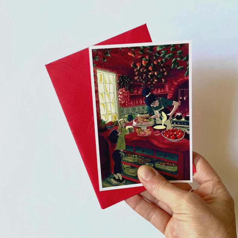 May include: A red envelope and a greeting card featuring a kitchen scene with two people. The card shows a person preparing food with another person looking on. The kitchen is decorated in red tones, with a window and shelves.