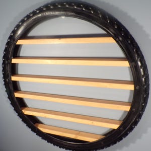 May include: A circular wall shelf made from a repurposed black tire. The shelf features several horizontal wooden slats, creating a unique and rustic storage solution. The tire's tread is visible, adding texture.
