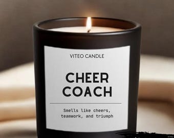 May include: A black glass candle with a white label featuring the text VITEO CANDLE, CHEER COACH, and Smells like cheers, teamwork, and triumph. The candle has a lit wick and a white wax surface. A black graphic in the corner reads GIFT BOX INCLUDED.
