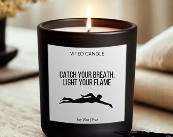 May include: A matte black candle in a glass jar with a white label featuring the text VITEO CANDLE, CATCH YOUR BREATH, LIGHT YOUR FLAME, a silhouette of a swimmer, and the text Soy Wax | 9 oz. A lit wick is visible at the top of the candle.