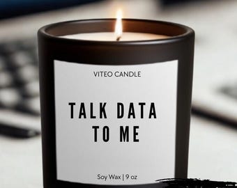 May include: A matte black candle in a glass jar with a white label featuring the text VITEO CANDLE, TALK DATA TO ME, and Soy Wax | 9 oz. A lit wick is visible at the center. A black graphic in the corner contains the text GIFT BOX INCLUDED.