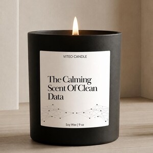 May include: A matte black candle in a cylindrical container with a lit wick. The white label reads VITEO CANDLE, The Calming Scent Of Clean Data, and Soy Wax | 9 oz, featuring a black geometric network graphic at the bottom of the label.