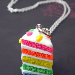 May include: A silver chain necklace with a colorful layered cake charm. The cake is decorated with sprinkles and frosting.