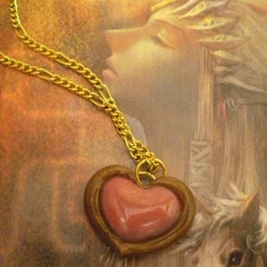 May include: A gold chain necklace with a heart-shaped pendant. The pendant is made of brown metal and has a pink heart-shaped stone in the center.