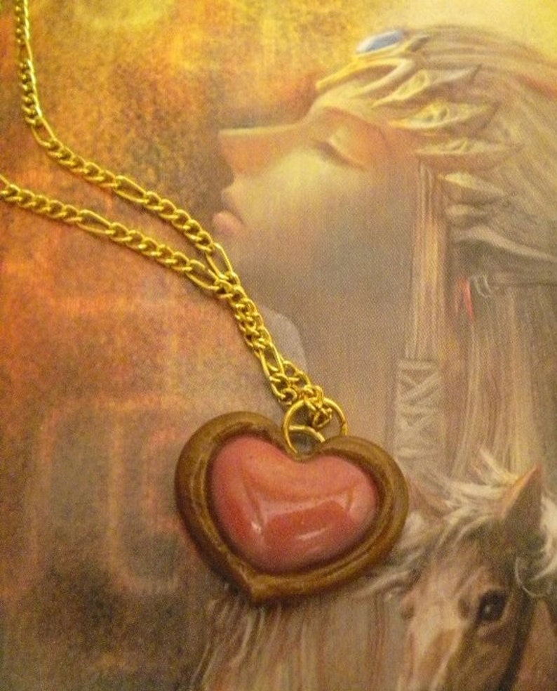 May include: A gold chain necklace with a heart-shaped pendant. The pendant is made of brown metal and has a pink heart-shaped stone in the center.