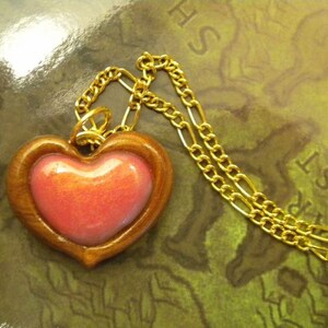 May include: A gold chain necklace with a wooden heart pendant. The heart has a pink, iridescent center.