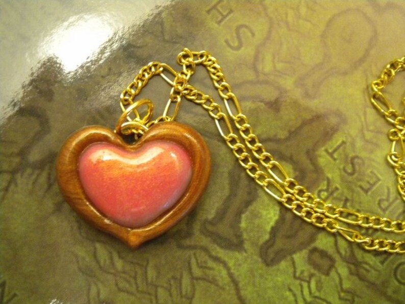 May include: A gold chain necklace with a wooden heart pendant. The heart has a pink, iridescent center.