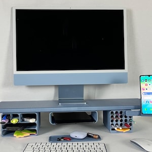 Puede incluir: Un monitor de ordenador azul claro se encuentra sobre un organizador de escritorio a juego con compartimentos para bolígrafos, un teléfono y otros útiles de oficina. Un teclado y un ratón inalámbricos están delante.