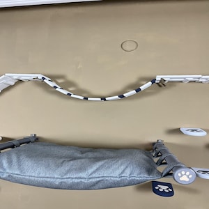 Può includere: Un set di mobili per gatti a parete con un letto imbottito grigio, un ponte di corda a strisce blu e bianche e piattaforme bianche. Il set include pali di supporto grigi e accenti a forma di zampa.