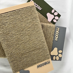 Op de afbeelding: Drie krabpalen voor katten. Elke krabpaal is omwikkeld met natuurlijk gekleurd touw. De uiteinden zijn beige, olijfgroen en grijs met het woord "meow" en een pootafdrukontwerp. De krabpalen zijn ontworpen voor katten.
