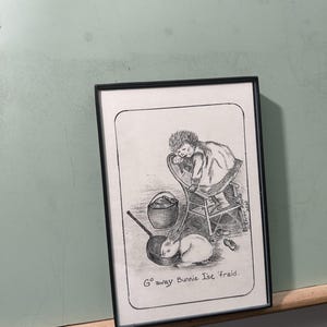 May include: Black and white framed illustration featuring a child and a rabbit. The child is seated on a chair, and the rabbit is in a pan. The text "Go away Bunnie I'se 'fraid" is at the bottom. The artwork is in a black frame.