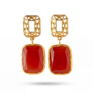 May include: A pair of gold-tone drop earrings featuring a rectangular open-work lattice top section connected to a large, faceted, rectangular red stone pendant with a textured gold-tone border, presented against a plain white background.