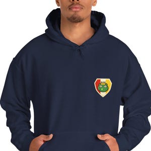 May include: Navy blue hooded sweatshirt with a front pocket and a small emblem on the chest. The emblem features a green frog with a crown inside a red and yellow shield. The sweatshirt is made of a soft material.