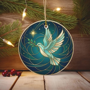 May include: Round Christmas ornament featuring a stained-glass style dove carrying an olive branch. The dove is teal and white, set against a teal and navy blue background with gold accents. A star and other small stars are also visible.