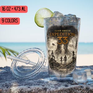 May include: A clear plastic tumbler with a lid and straw, filled with ice and a lime wedge. The tumbler features the text "CLAIR OBSCUR EXPEDITION 33" and a black and white graphic. The tumbler holds 16 oz.