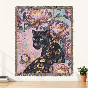 May include: A woven throw blanket featuring a black panther with gold spots surrounded by large, detailed purple and pink peony flowers against a light blue background. The blanket has a fringed edge on the top and bottom, with a textured finish.
