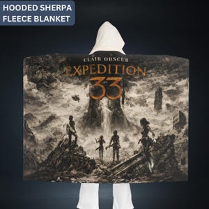 May include: A hooded sherpa fleece blanket featuring a detailed black and white illustration with the text "CLAIR OBSCUR EXPEDITION 33". The design depicts figures in a landscape with a waterfall and ruins. The hood is white.