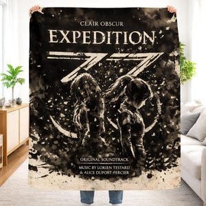 May include: A large, rectangular blanket with a sepia-toned design. The blanket features the words "CLAIR OBSCUR EXPEDITION" in bold, black letters. Below the title is a stylized illustration of two figures. The words "ORIGINAL SOUNDTRACK" and the names of the composers are also visible.