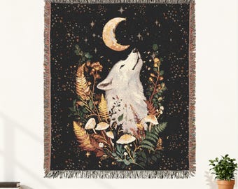 May include: A woven throw blanket featuring a black background with a white wolf howling at a crescent moon. The design includes detailed illustrations of ferns, mushrooms, and foliage in earthy tones, surrounded by a field of small golden stars.