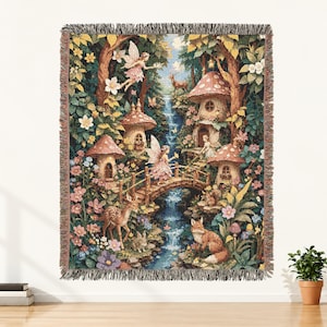 May include: A woven tapestry throw blanket featuring a detailed forest scene with fairies, mushroom-shaped houses, a waterfall, a wooden bridge, a deer, a fox, and a rabbit, all surrounded by colourful flowers and lush green foliage with fringed edges.