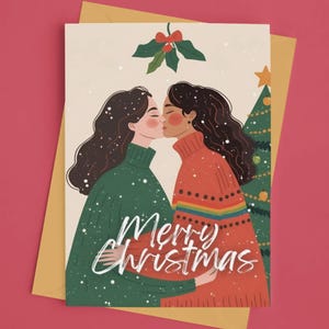 以下が含まれることがあります： 緑とオレンジのセーターを着た、キスをしている女性2人のイラストが描かれたクリスマスカード。「Merry Christmas」の文字が筆記体で書かれており、上部にはヒイラギの枝があります。背景にはクリスマスツリーが見えます。