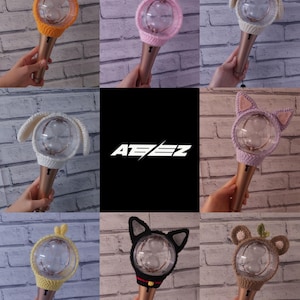 May include: A collection of handmade crochet light stick covers in various animal designs, including bear, bunny, and cat ears. The covers are in shades of orange, pink, white, yellow, black, and brown. The logo "ATEEZ" is displayed in white on a black background.