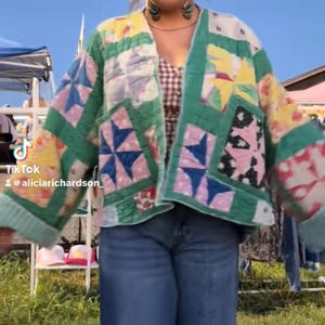 May include: A long-sleeved quilted jacket featuring a patchwork design with various star patterns in shades of green, yellow, pink, and white. The jacket has a green border, an open front, and is worn over a brown and white gingham top and blue jeans.