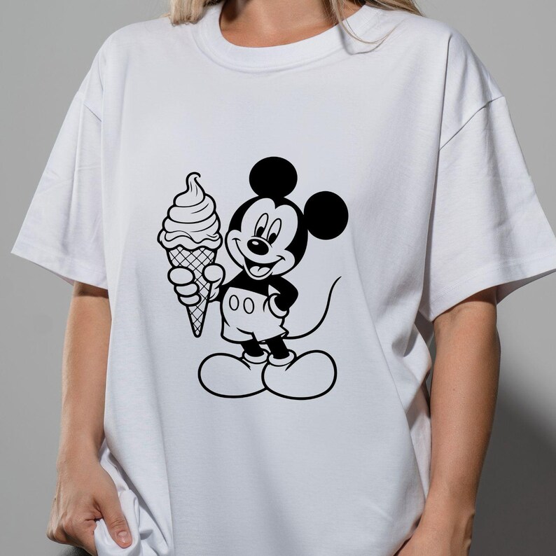 May include: White t-shirt featuring a black and white graphic of Mickey Mouse holding an ice cream cone. The cartoon character is smiling. The shirt has short sleeves and a crew neck.