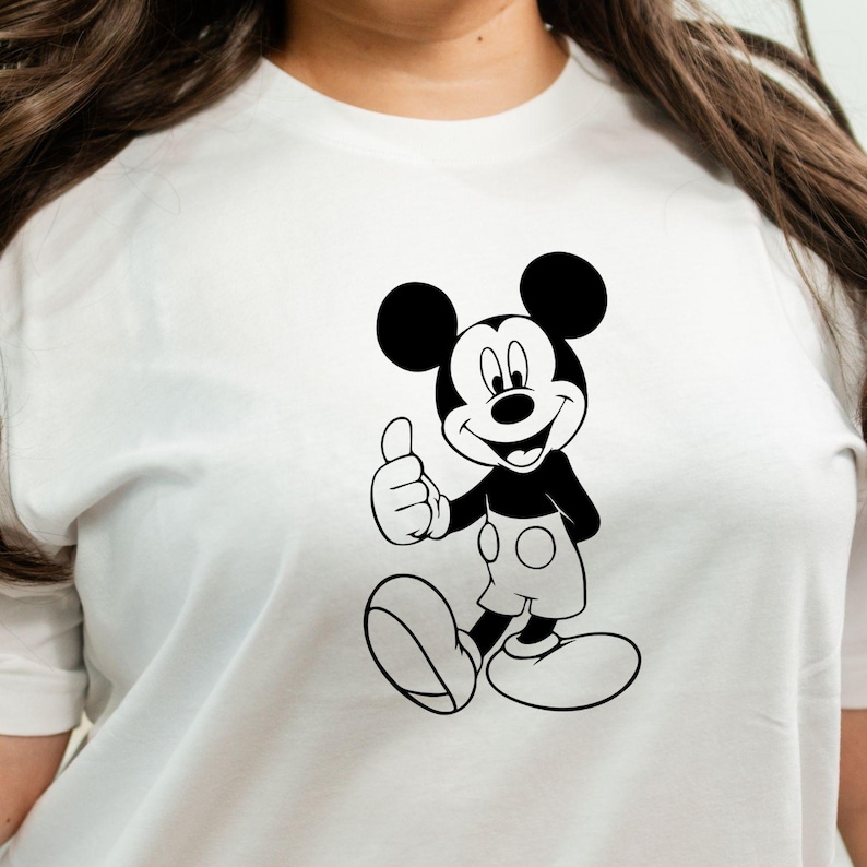 May include: White t-shirt featuring a black and white illustration of Mickey Mouse giving a thumbs-up. The cartoon character is smiling and wearing shorts and large shoes. The shirt has short sleeves.