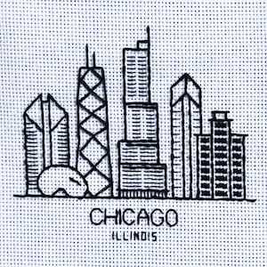 Könnte beinhalten: Schwarz-weiß gestickte Skyline von Chicago, Illinois. Das Design zeigt stilisierte Wolkenkratzer und den Namen der Stadt darunter gestickt. Das Kunstwerk befindet sich auf einem weißen, gepunkteten Stoff.
