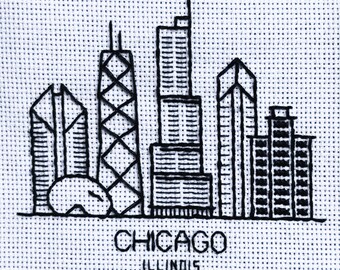 以下が含まれることがあります： イリノイ州シカゴの白黒刺繍都市景観。 デザインは様式化された高層ビルと都市名を刺繍で表現しています。 このアートワークは、白い点線模様の生地に施されています。