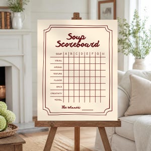 May include: A cream-colored rectangular sign on a wooden easel featuring dark red text and grid lines. The sign reads Soup Scoreboard with categories for Visual, Aroma, Texture, Flavor, Spice, Creativity, and Total, plus The Winner line.