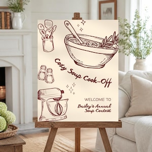 May include: A cream-colored sign on a wooden easel featuring dark red line art of a bowl of soup, a stand mixer, kitchen utensils, and salt and pepper shakers. The text reads: Cozy Soup Cook-Off, WELCOME TO Bailey's Annual Soup Contest.