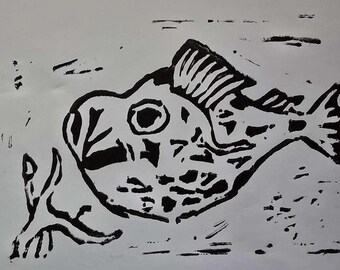 May include: A monochrome linocut print depicting a fish. The fish is rendered in black against a white background, with details like fins and scales. The print has a textured look.