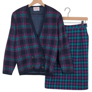 Puede incluir: Un conjunto de falda y chaqueta a cuadros vintage. El traje azul marino presenta un estampado de cuadros turquesa y morado. La chaqueta tiene cuello en V, diseño cruzado con botones dorados. La falda es de estilo lápiz.