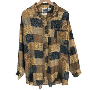 Peut inclure: Une chemise à manches longues boutonnée avec un motif patchwork dans des tons de marron, beige et bleu marine foncé. Le tissu présente divers motifs géométriques, floraux et linéaires. Une étiquette au col indique details express.